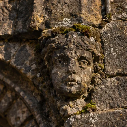 A small carved stone face in the wall of the old city gate, moss above it